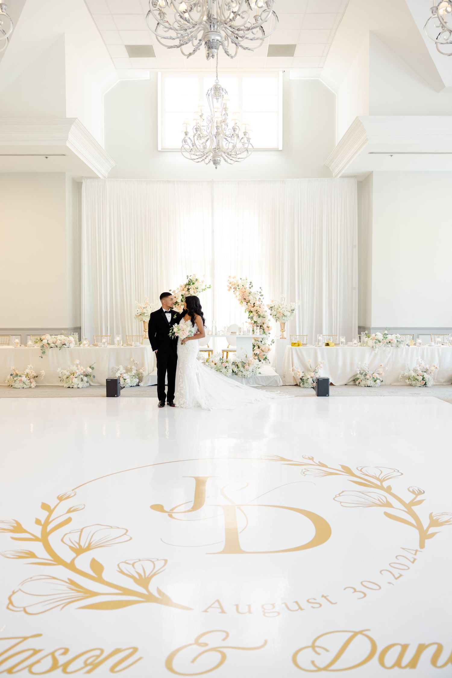 Wedding couple standing on custom gold monogram dance floor with elegant chandeliers above.