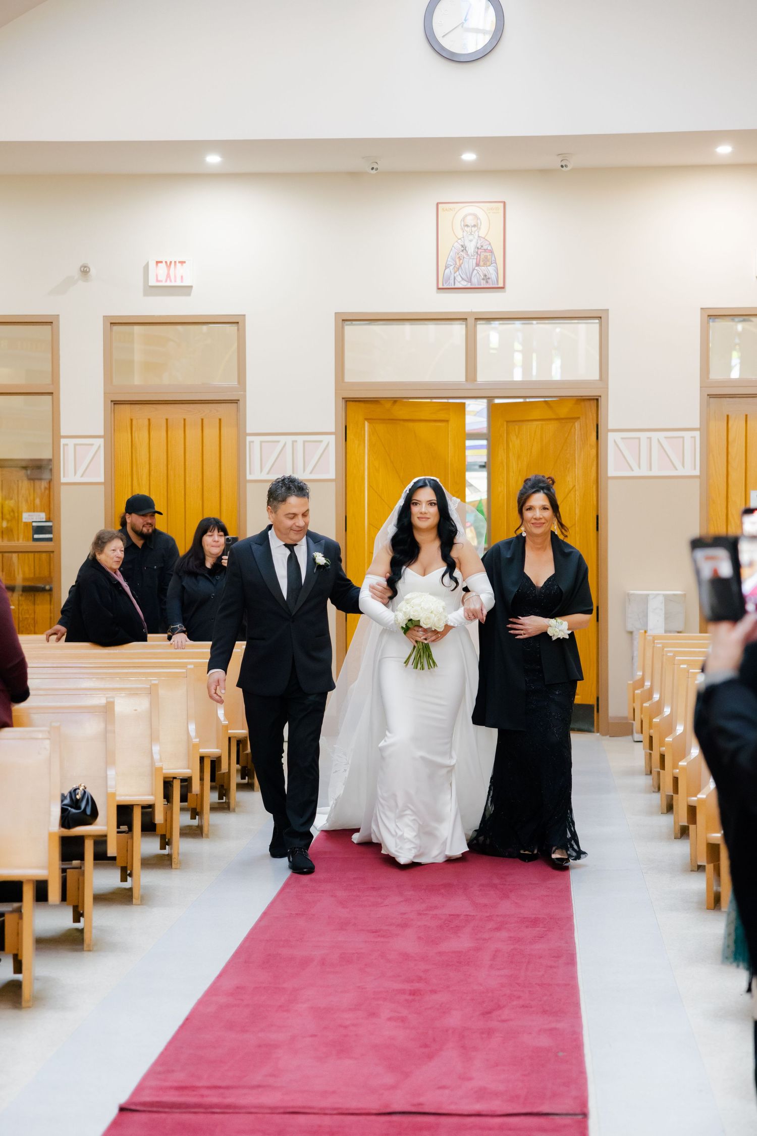 A wedding party proceeds down a red-carpeted church aisle during a ceremony.