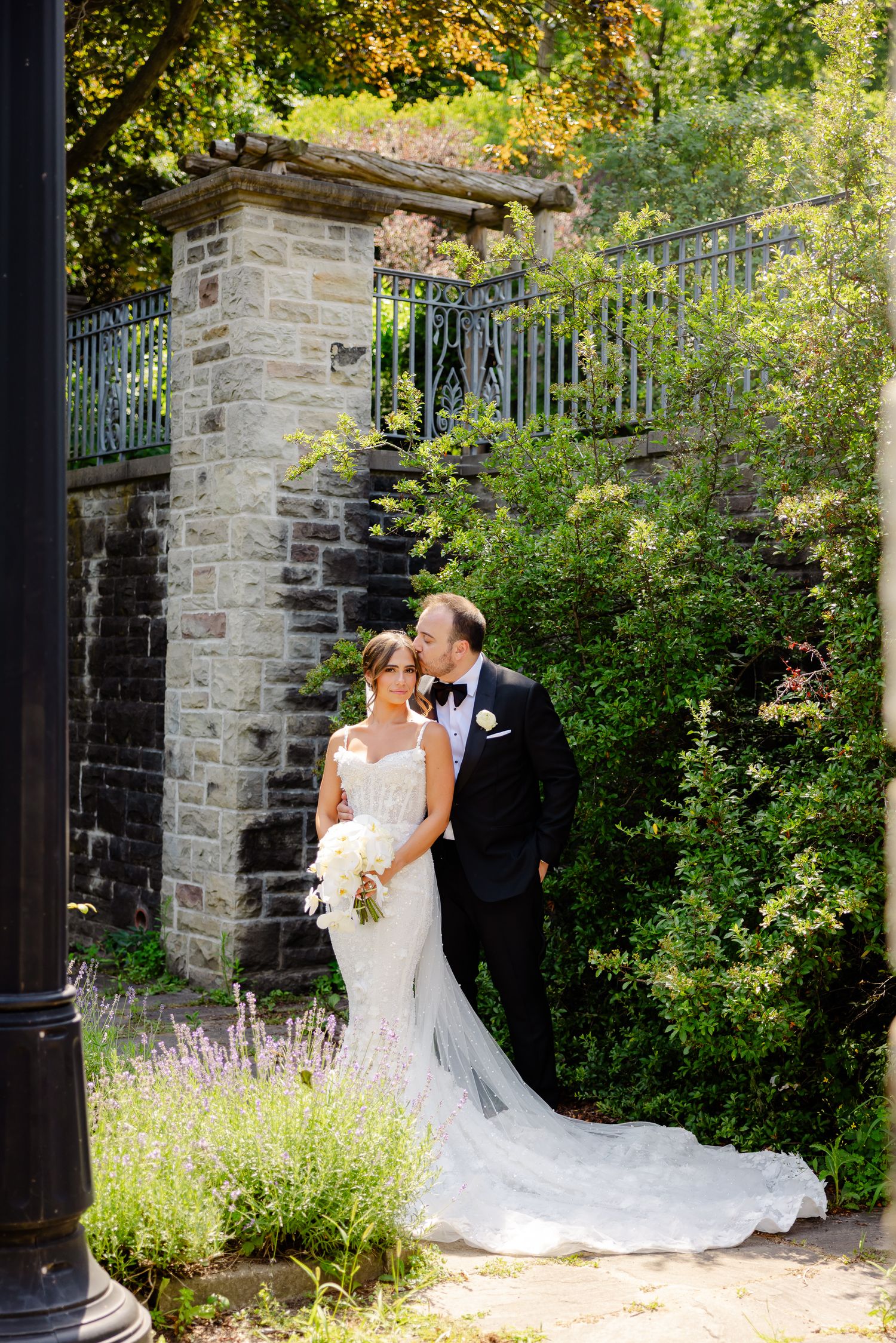 Elegant garden wedding photos showcasing a beautiful lace gown against stone pillars and lavender flowers.
