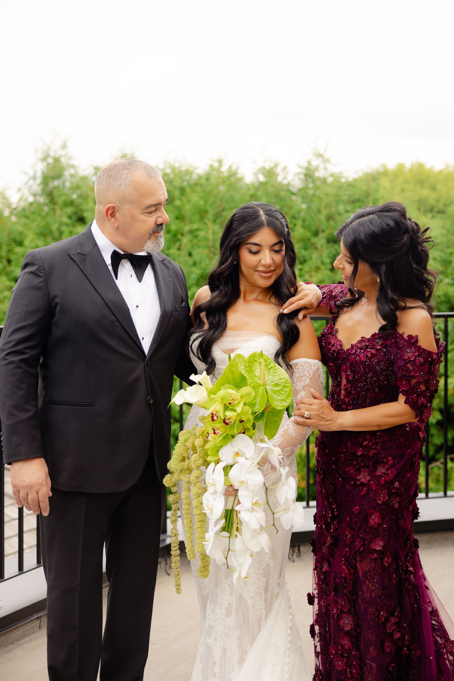 Wedding couple and wedding party member in burgundy dress share intimate moments during outdoor photo session.