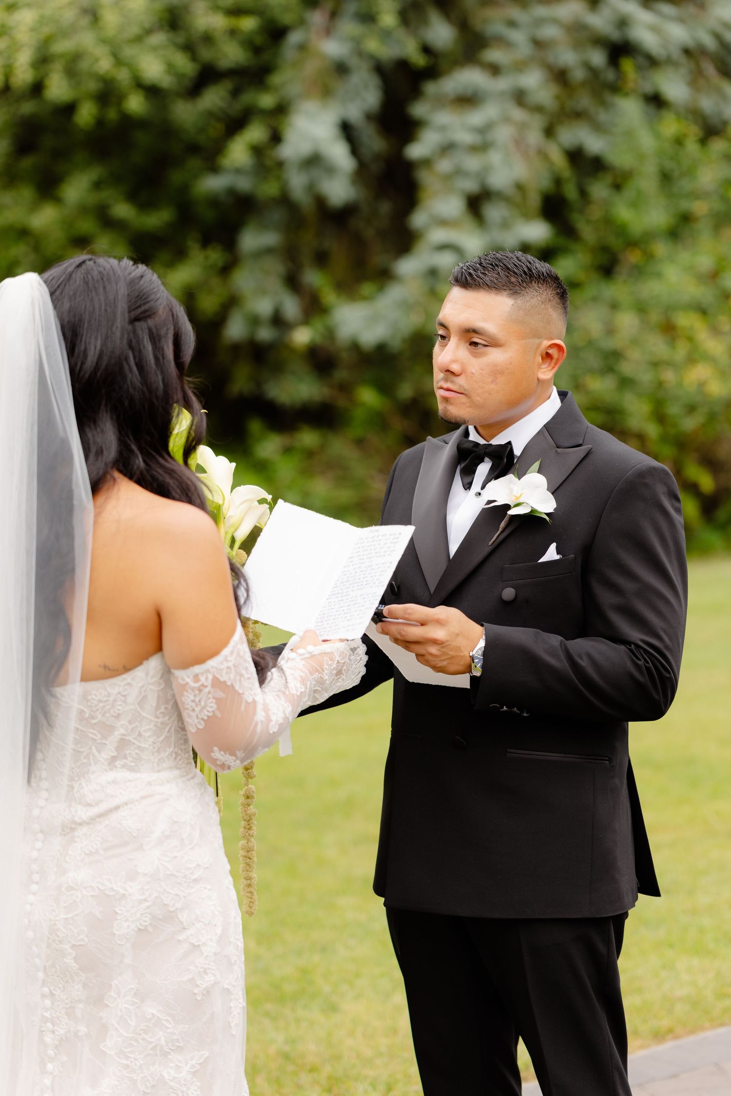 A bride and groom sharing a private moment while reading personal vows during an outdoor wedding.