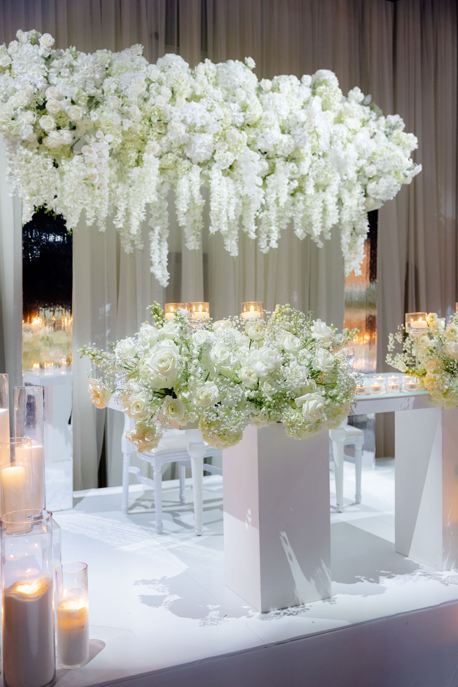 Stunning white floral arrangement with cascading flowers on modern white pedestals with candles.