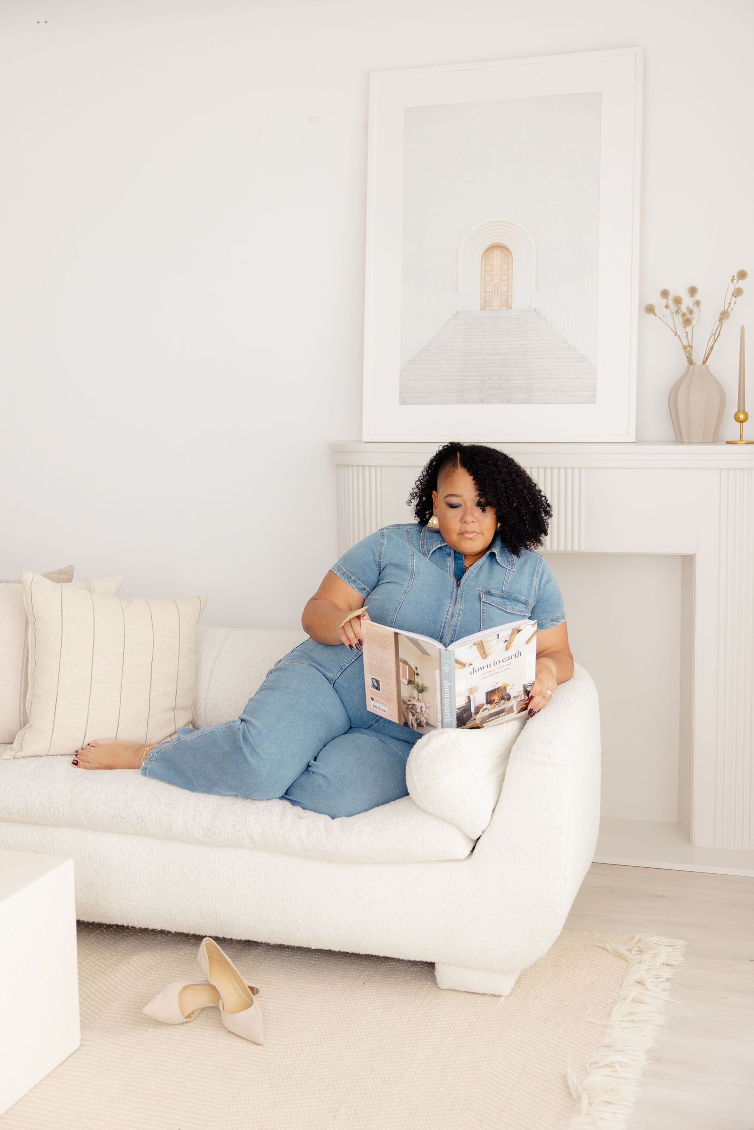 Someone relaxes on a white couch while reading a book in a minimalist living room with soft neutral decor.