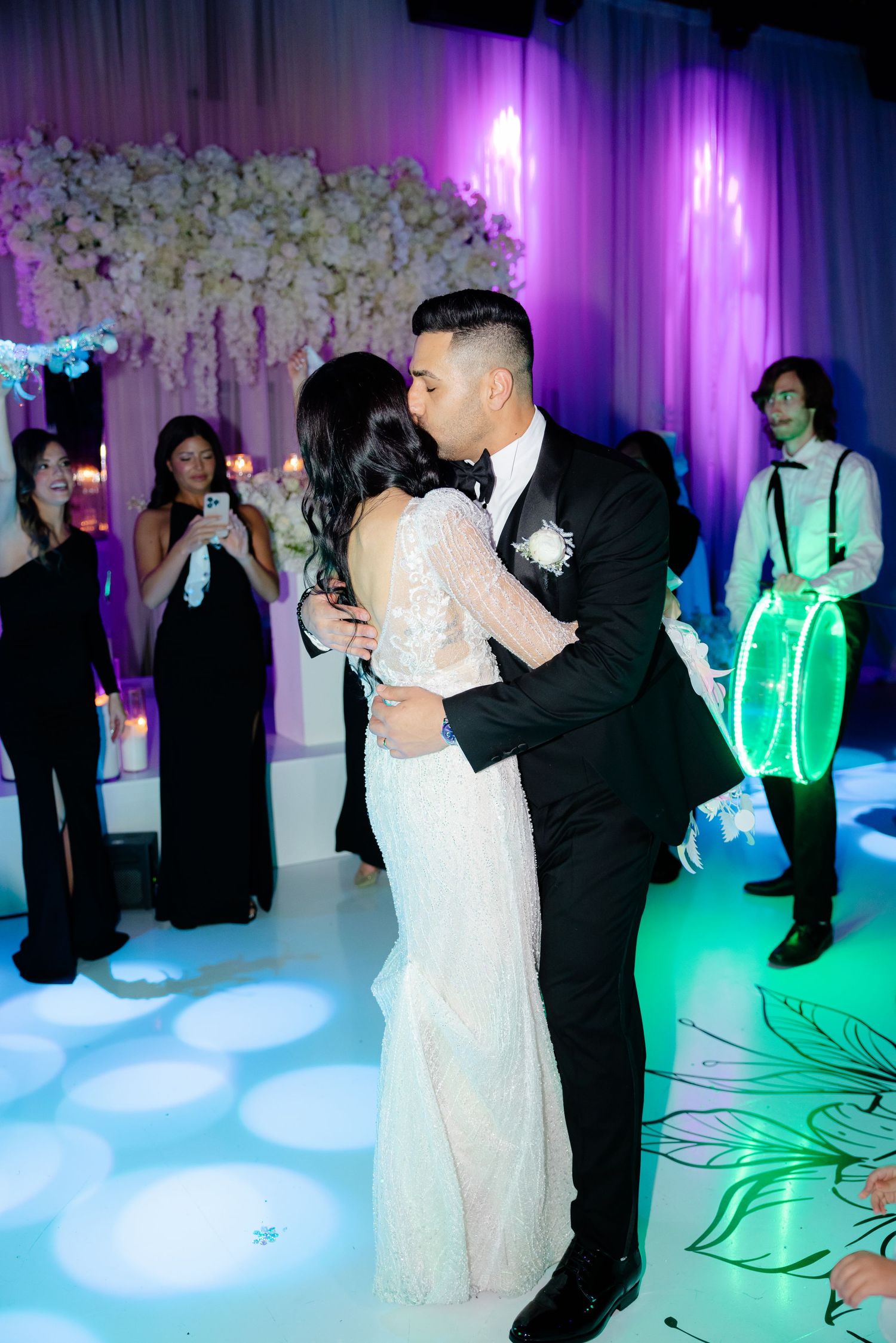 Romantic first dance at wedding reception with purple lighting and glowing LED performers in background.