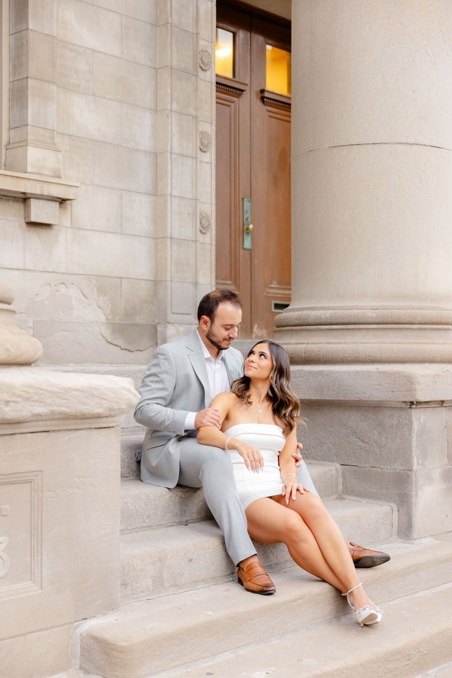 Intimate portrait on stone steps with classical architecture and warm lighting.