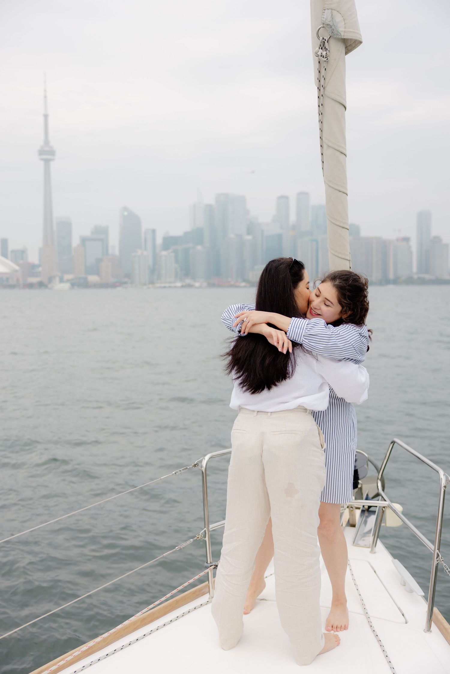 Two people embracing on a boat deck with Toronto's skyline visible across the water.