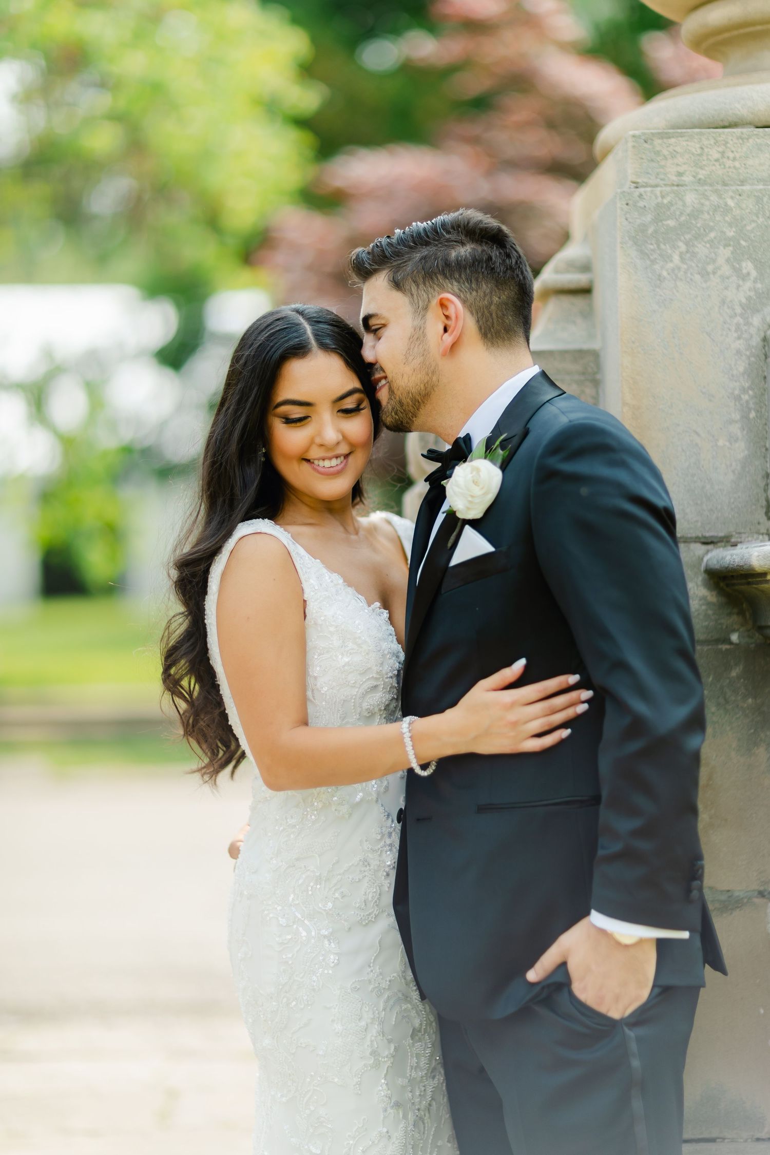 Candid wedding photo showing couple in elegant attire sharing joyful moment against garden backdrop.