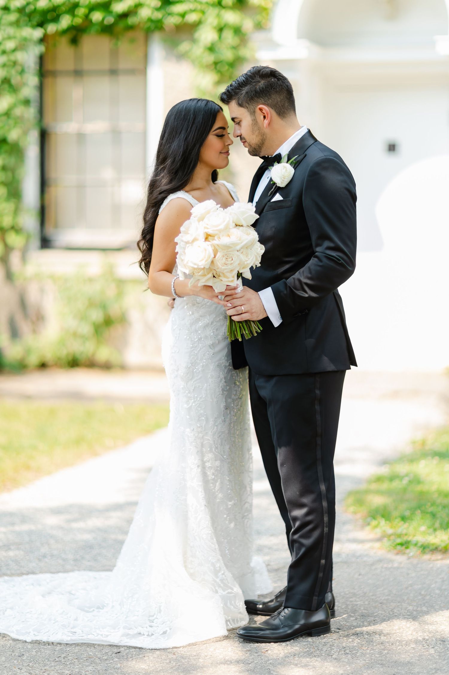 Romantic wedding portrait with a couple holding a white bouquet against an ivy backdrop.