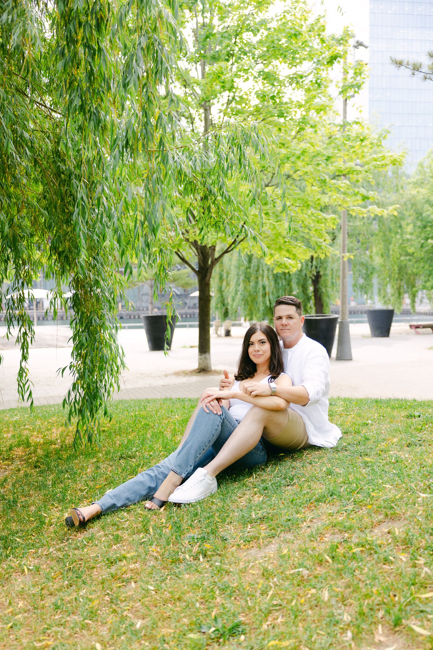Couple enjoying summer afternoon under drooping willow trees in city park.