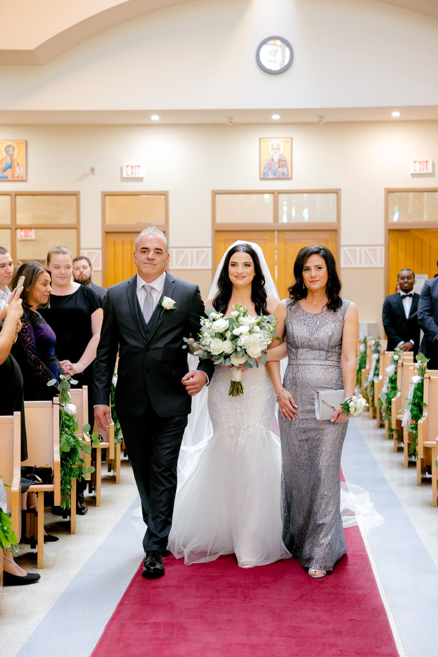 Wedding processional captured walking down a red-carpeted church aisle with pew decorations.