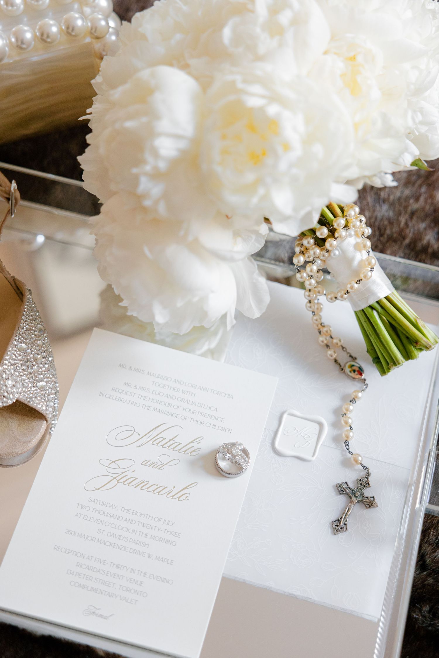 Lush white peony bouquet with decorative rosary beads beside elegant wedding stationery.