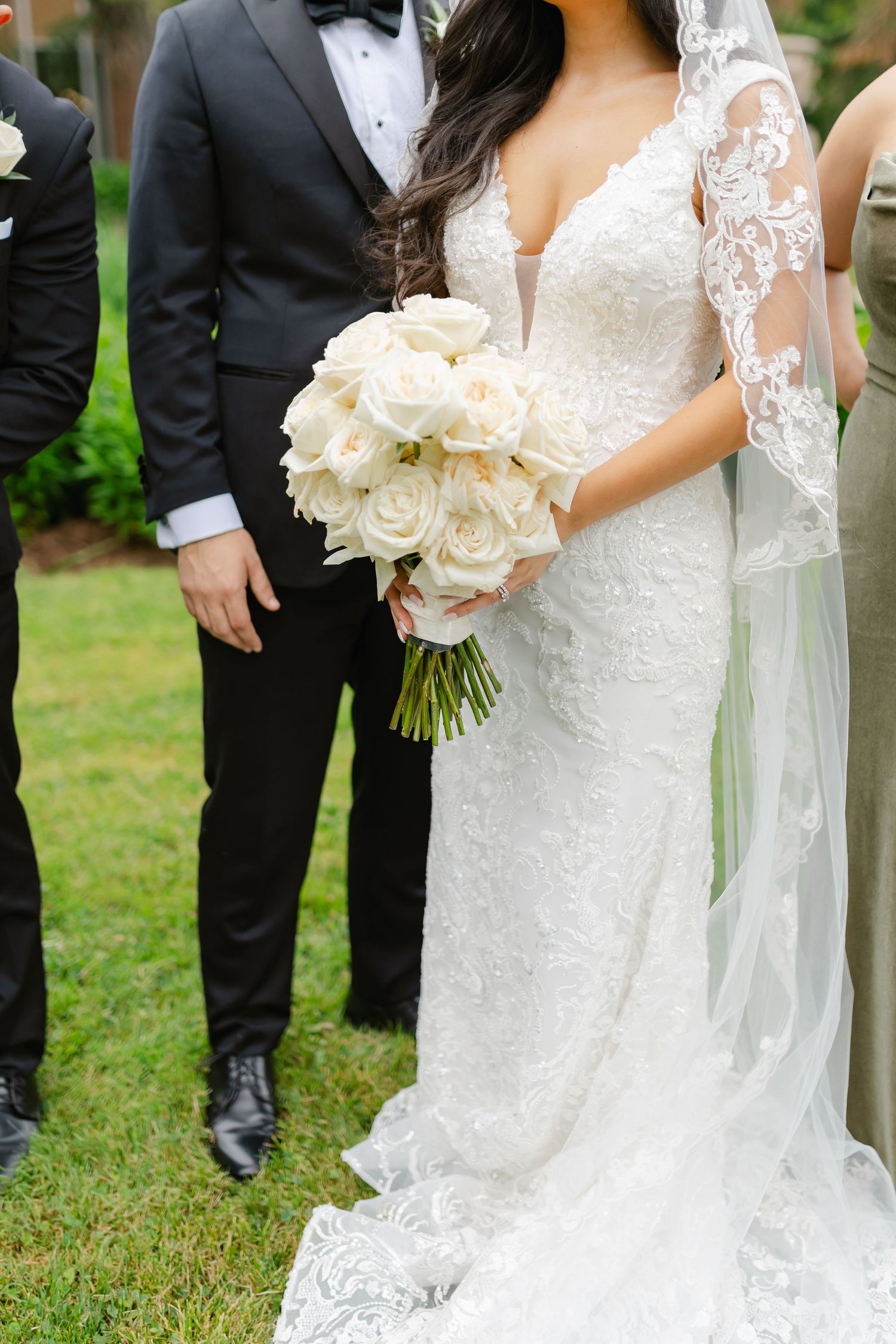 Close-up of a bridal bouquet with white roses held against a lace wedding dress.