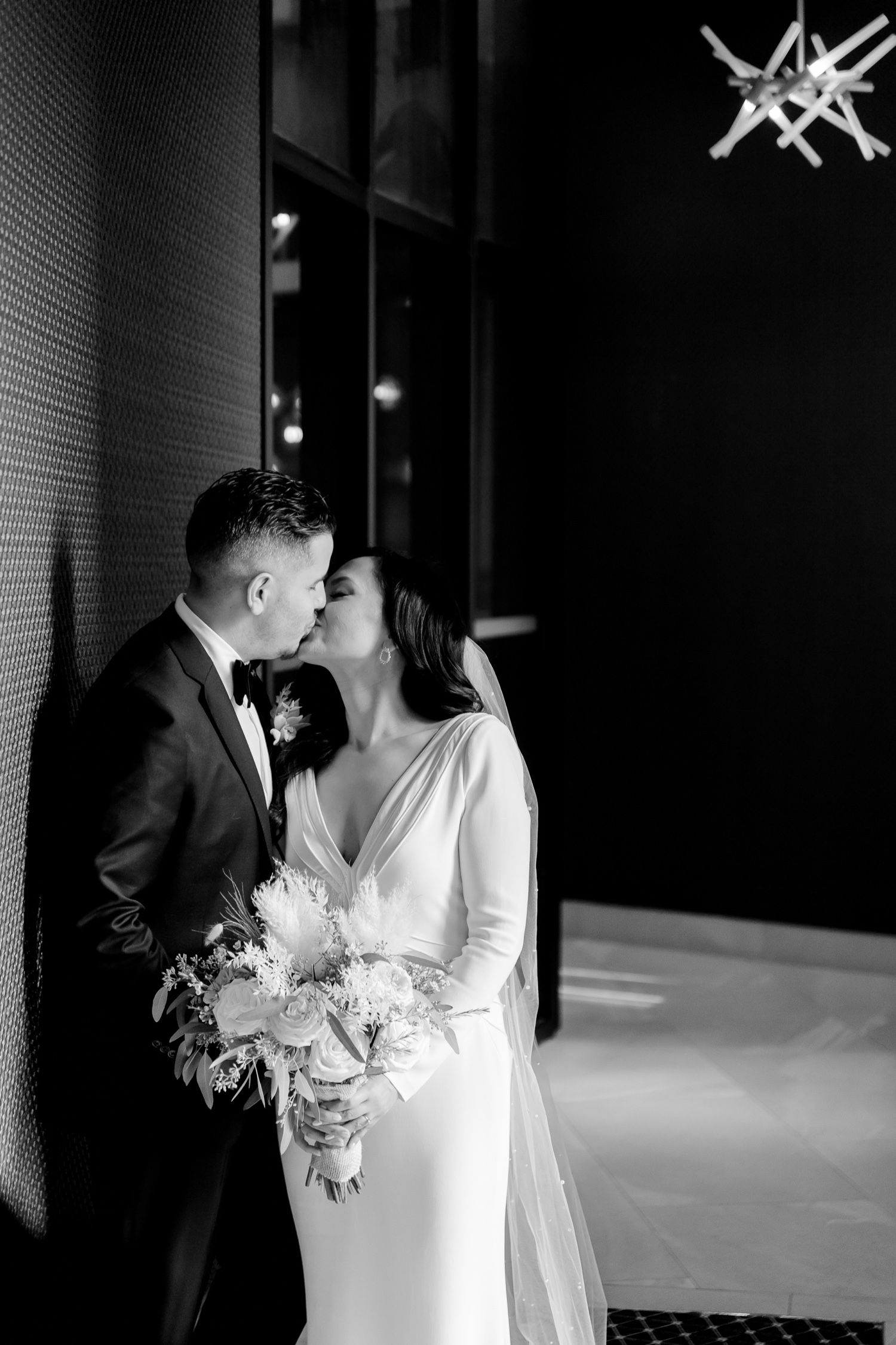 Dramatic black and white wedding portrait featuring a romantic moment against a textured wall.