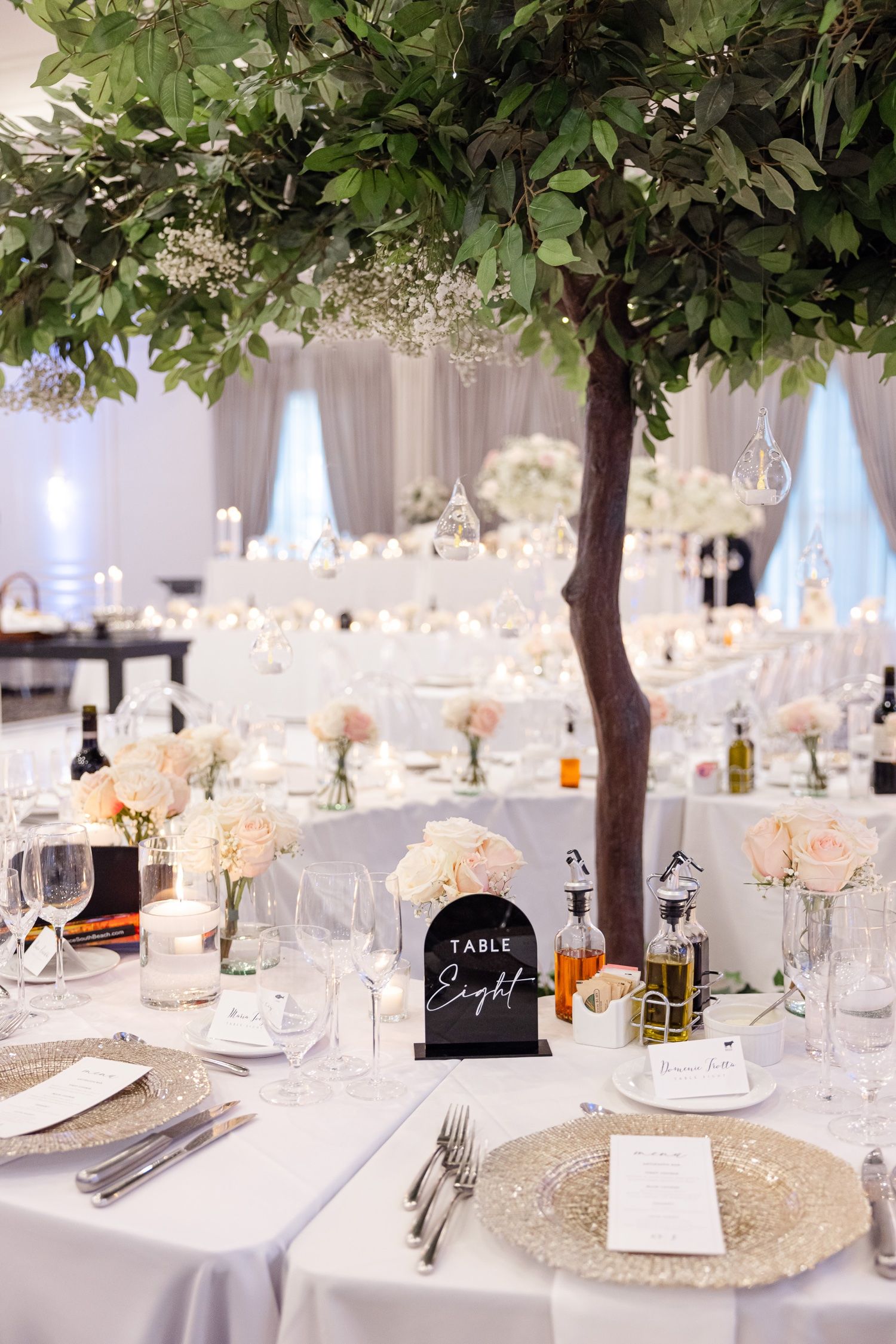 Wedding table setting with greenery tree centerpiece and white floral arrangements.