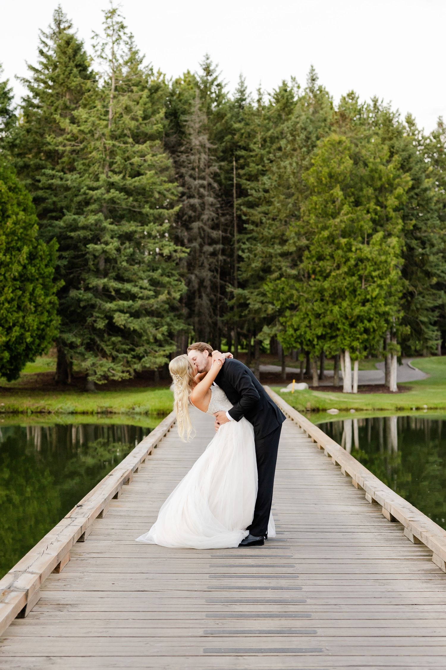 Romantic pose on wooden dock with evergreen forest and pond reflections.