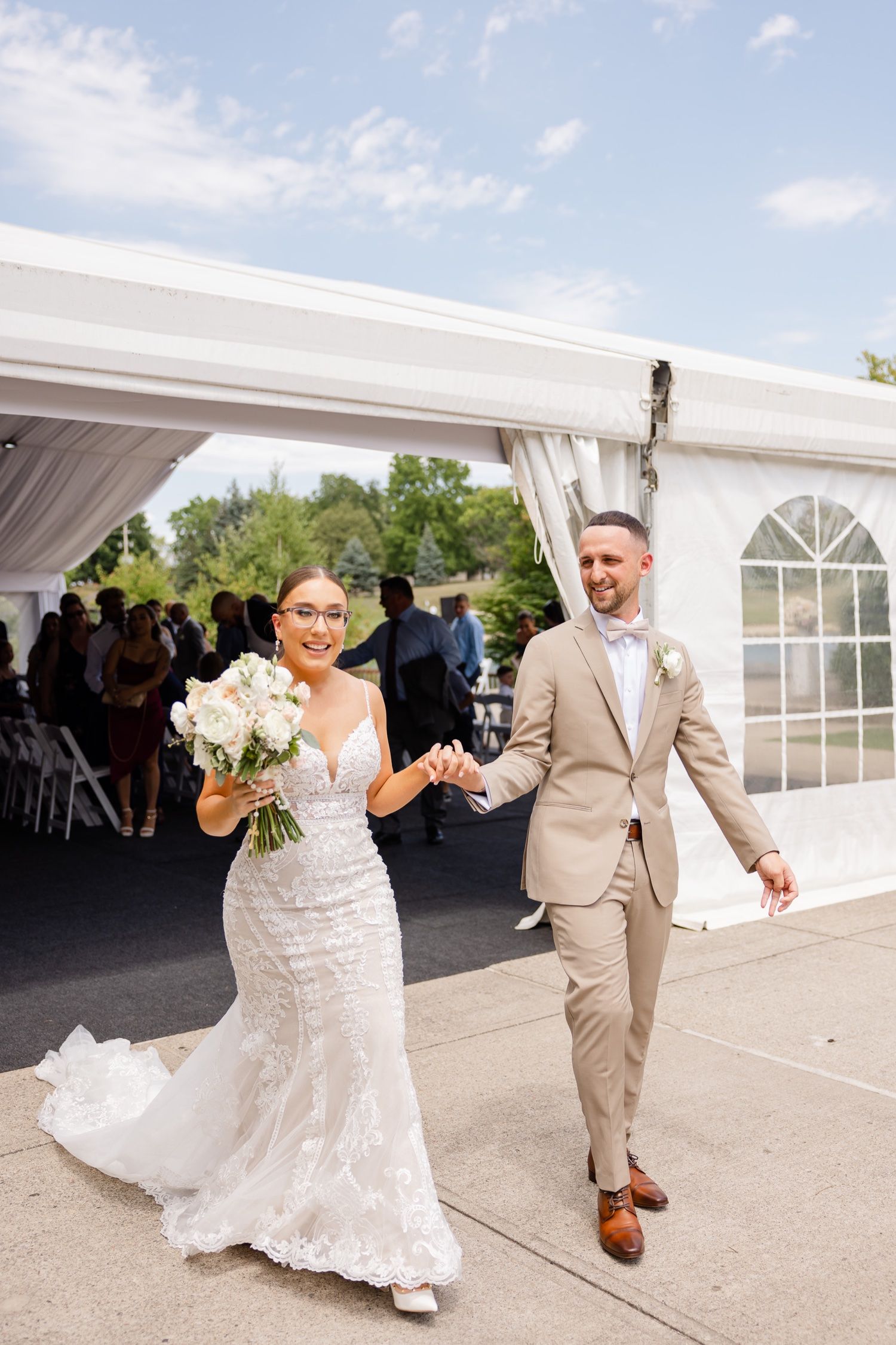 Joyful newlyweds exit their wedding ceremony under a white tent with bright natural lighting.