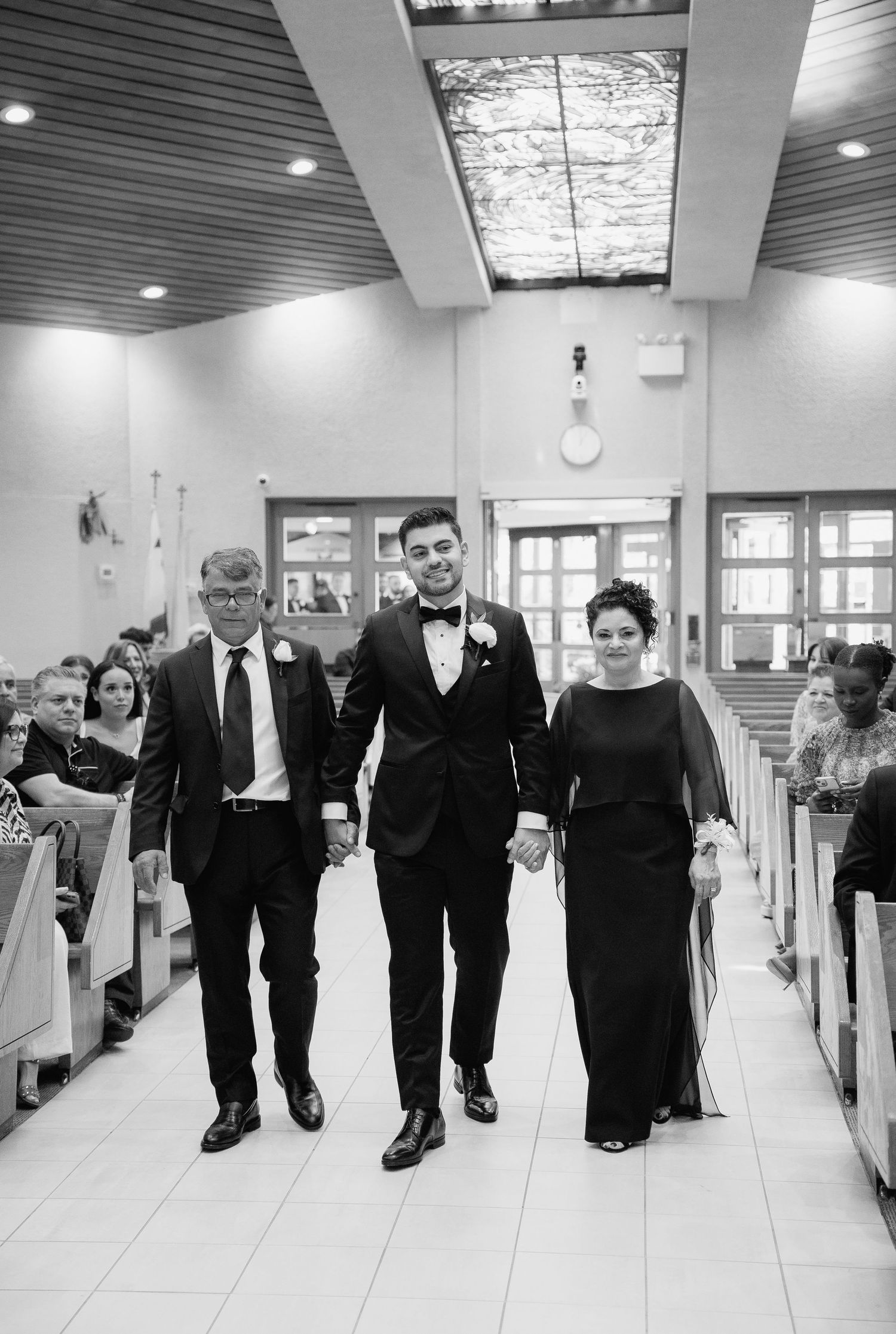 Black and white photo of wedding party walking down church aisle with decorative ceiling.