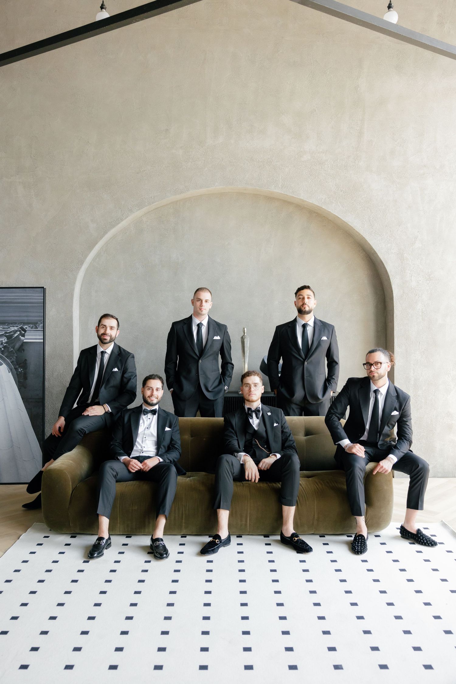 Stylish wedding party members posed on a tan couch with others standing behind.