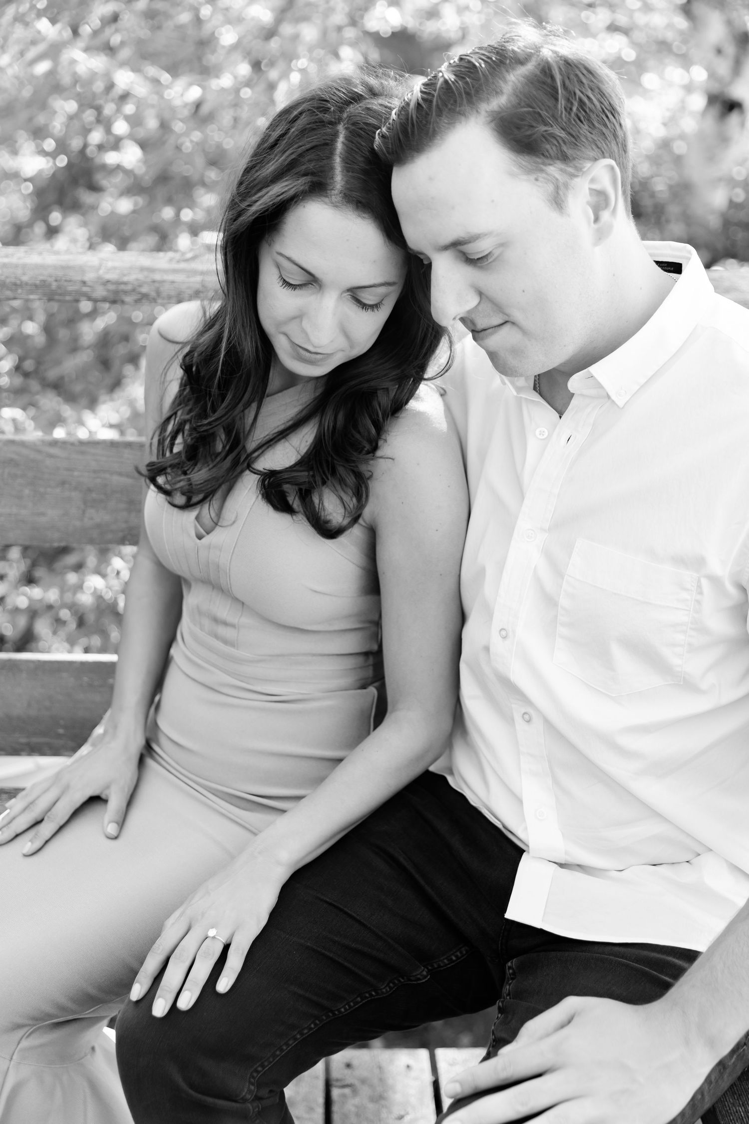 Black and white portrait of couple sharing intimate moment on wooden bench.