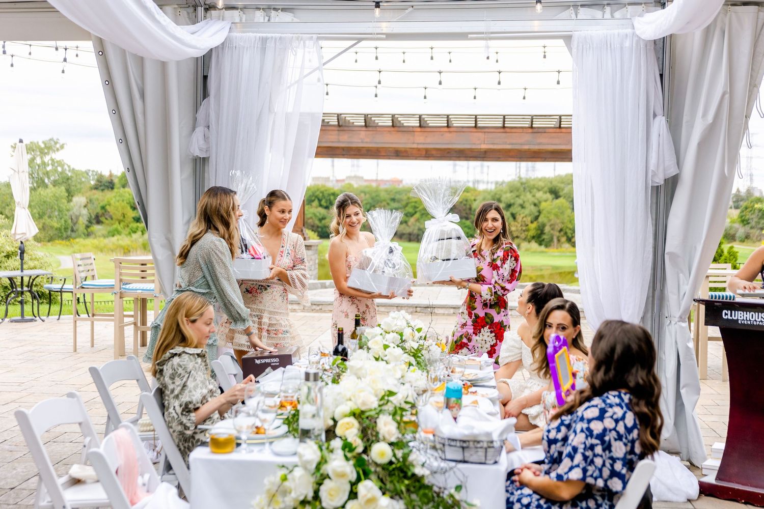Elegant outdoor celebration with guests seated at flower-decorated tables under white draping.