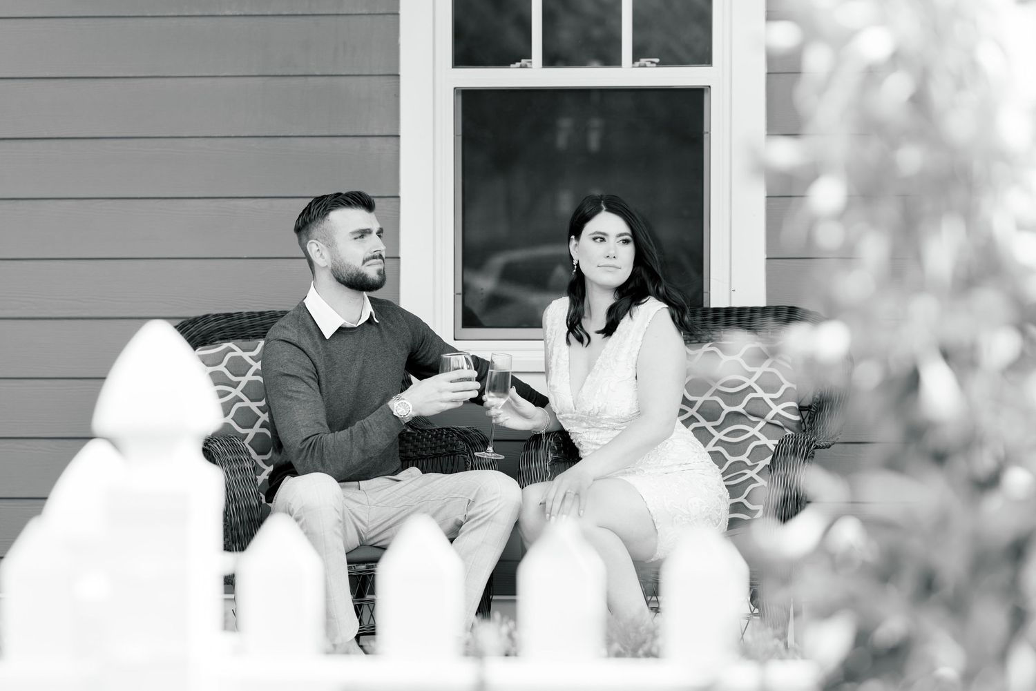 A black and white portrait of two people sharing drinks on an outdoor bench.