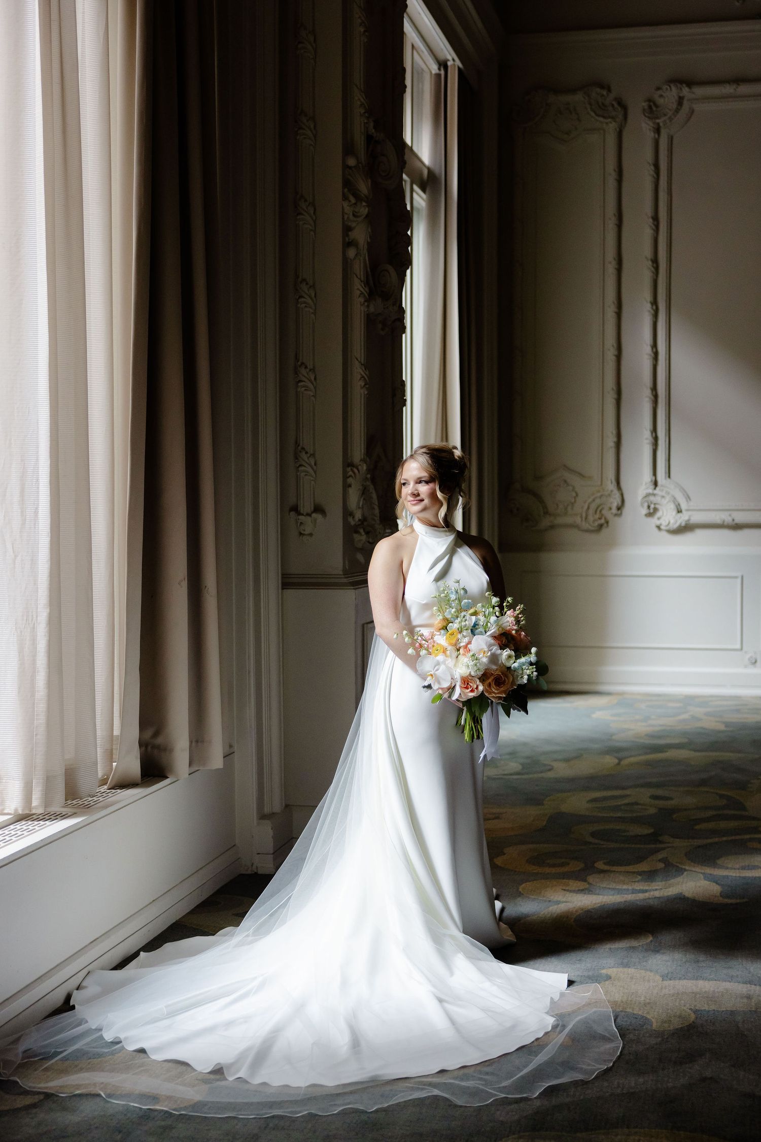 Wedding dress with long train photographed in elegant room with ornate moldings and natural window light.