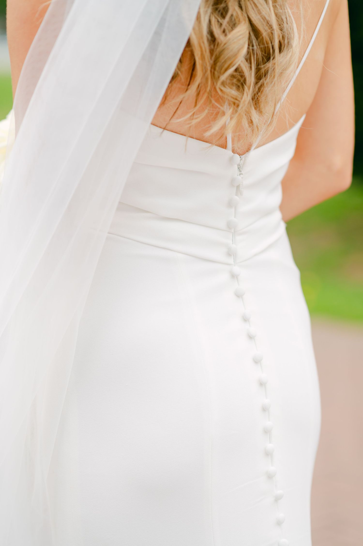 Close-up detail of white wedding dress buttons trailing down the back of an elegant bridal gown.