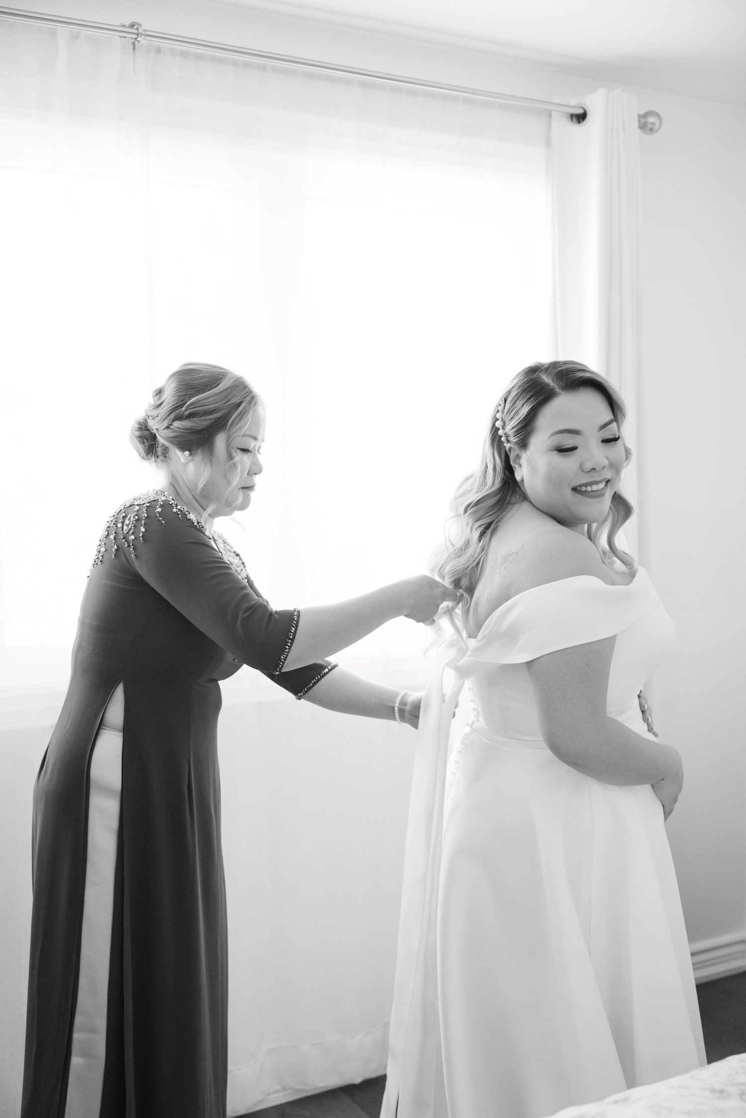 Black and white image of wedding dress fitting with helper adjusting back of gown.
