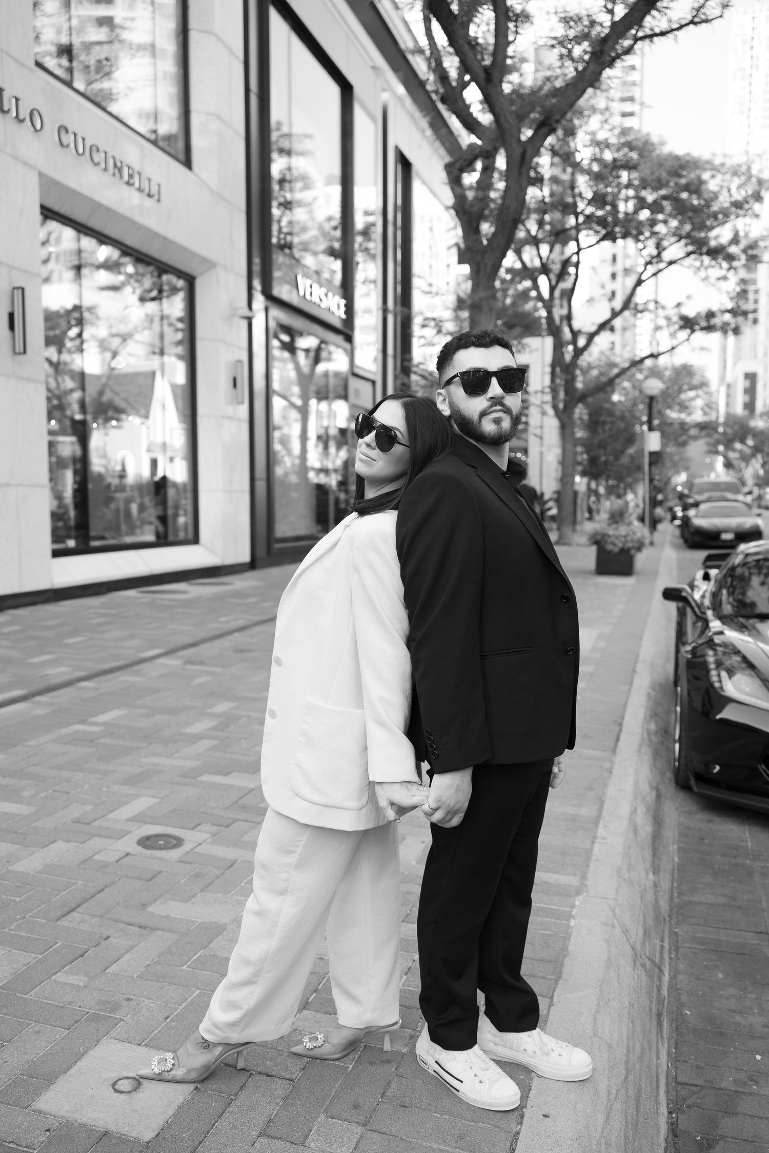 Fashionable couple in black and white outfits pose back-to-back on urban street.