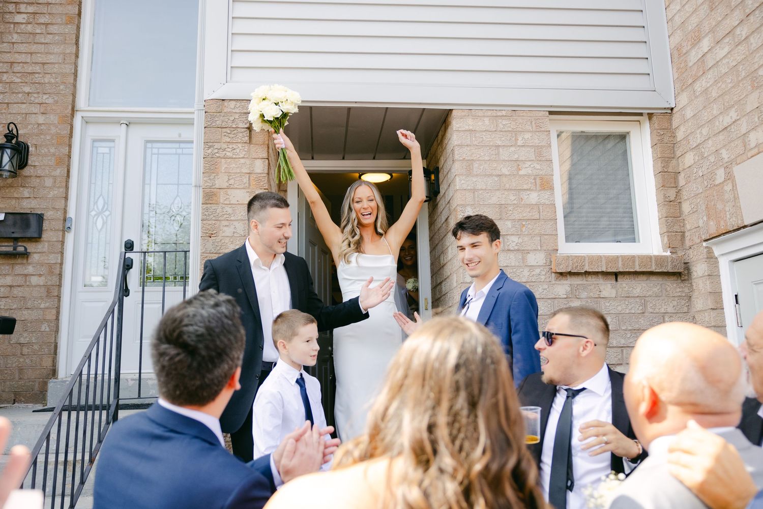 Celebratory moment with raised arms on porch steps surrounded by wedding guests.