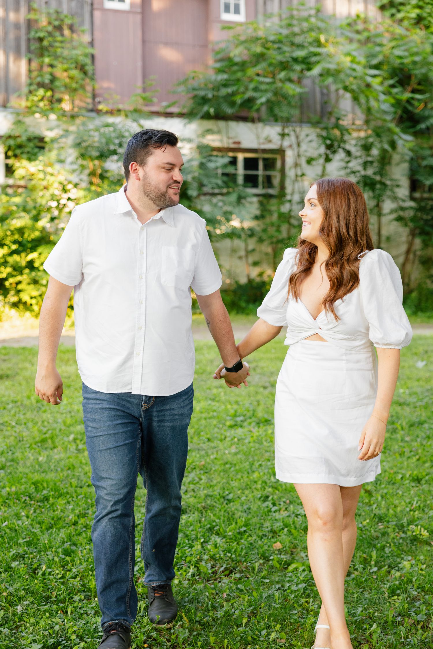 Couple taking a romantic stroll on grass with a rustic building backdrop.