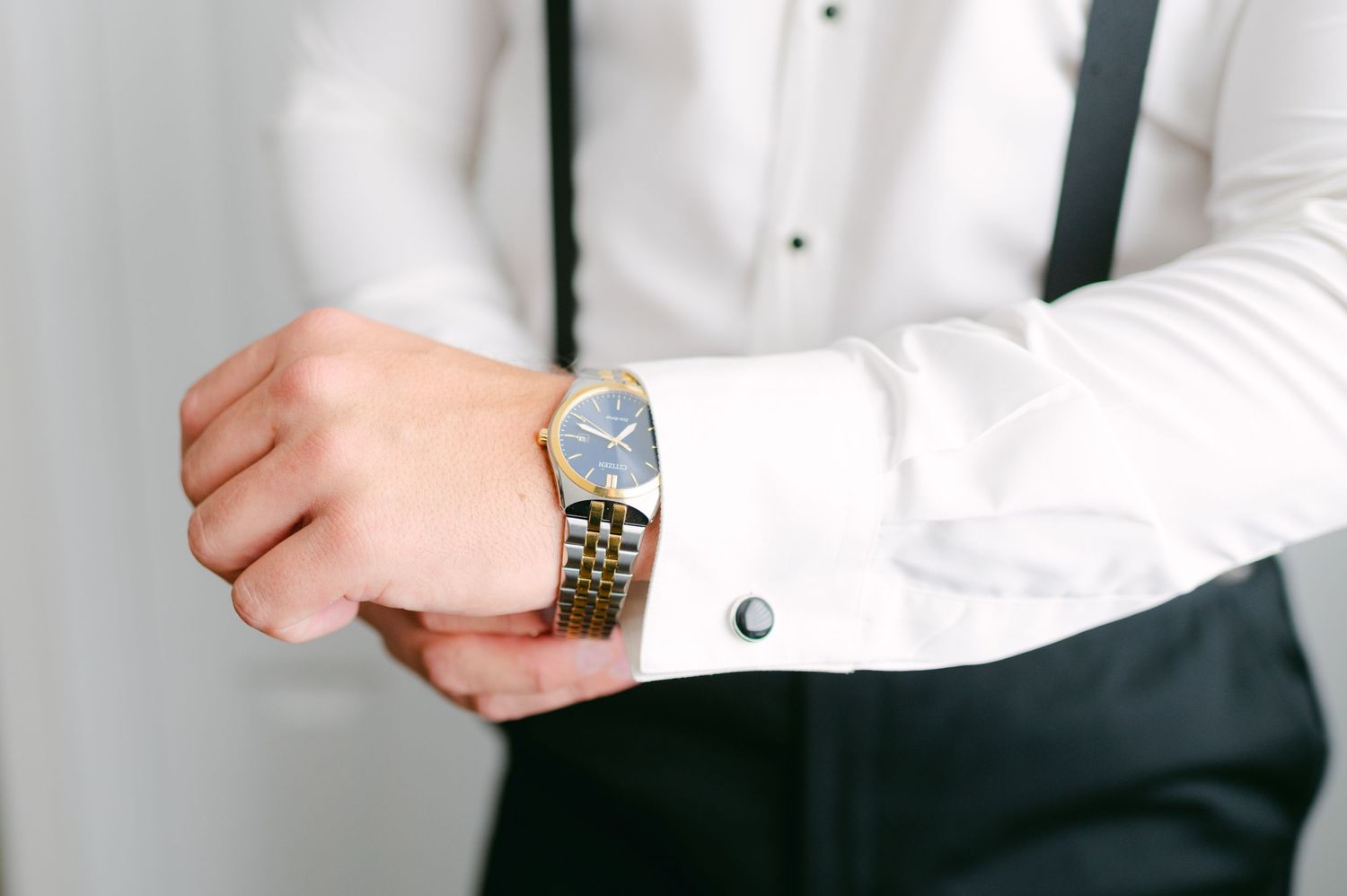 Close up of a silver and gold dress watch being adjusted on a formal white shirt cuff.