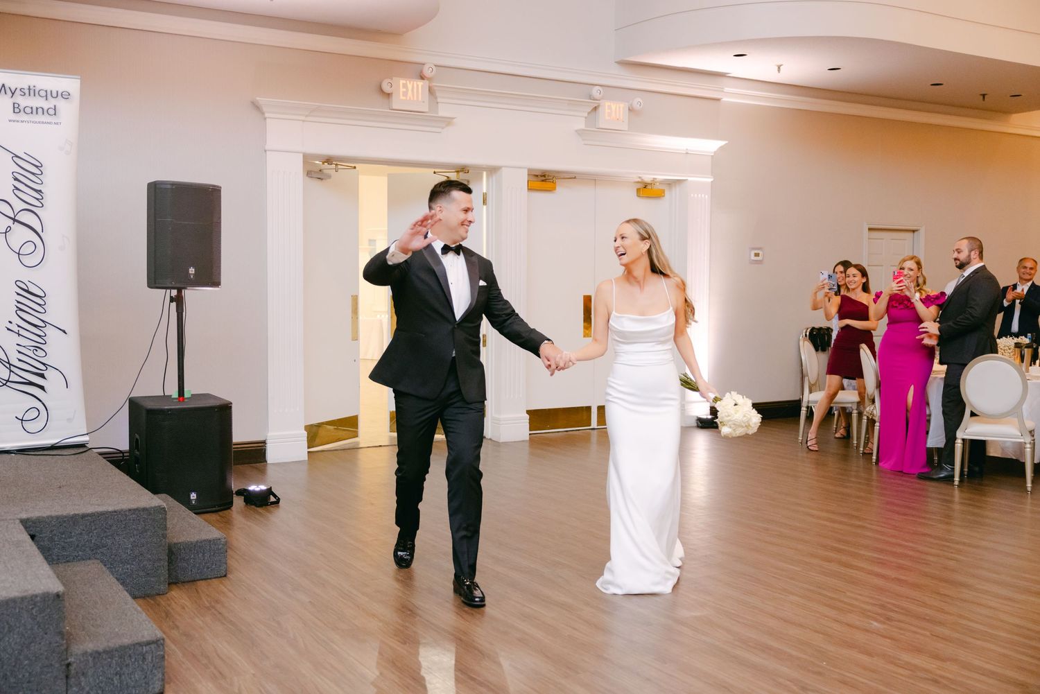 Dancing couple celebrating during wedding reception in elegant white-walled venue with hardwood floors.