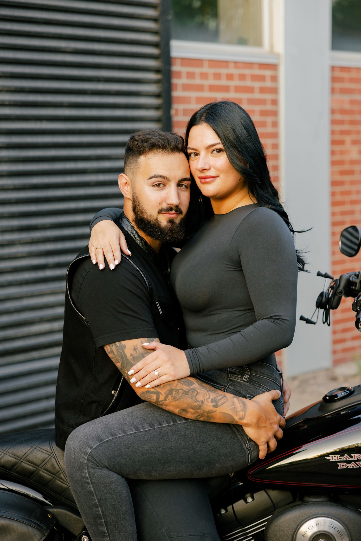 A couple poses together on a motorcycle during a casual outdoor photoshoot.