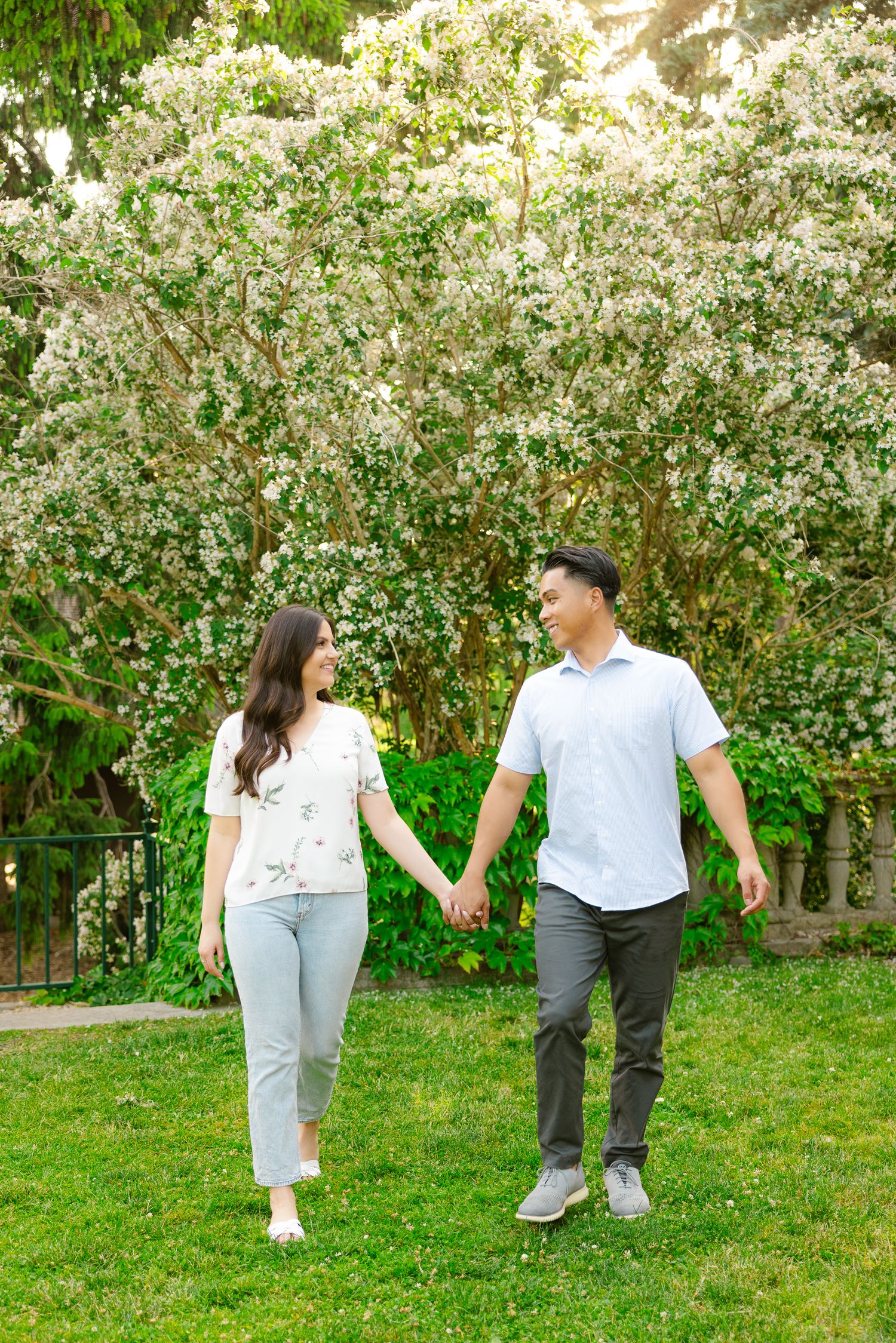 Couple walking through a garden holding hands with flowering trees in background.