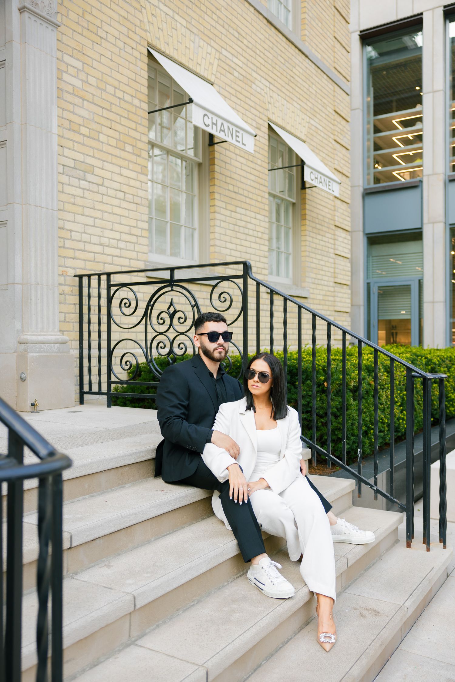 Trendy couple in contrasting suits relaxing on steps of luxury retail store.