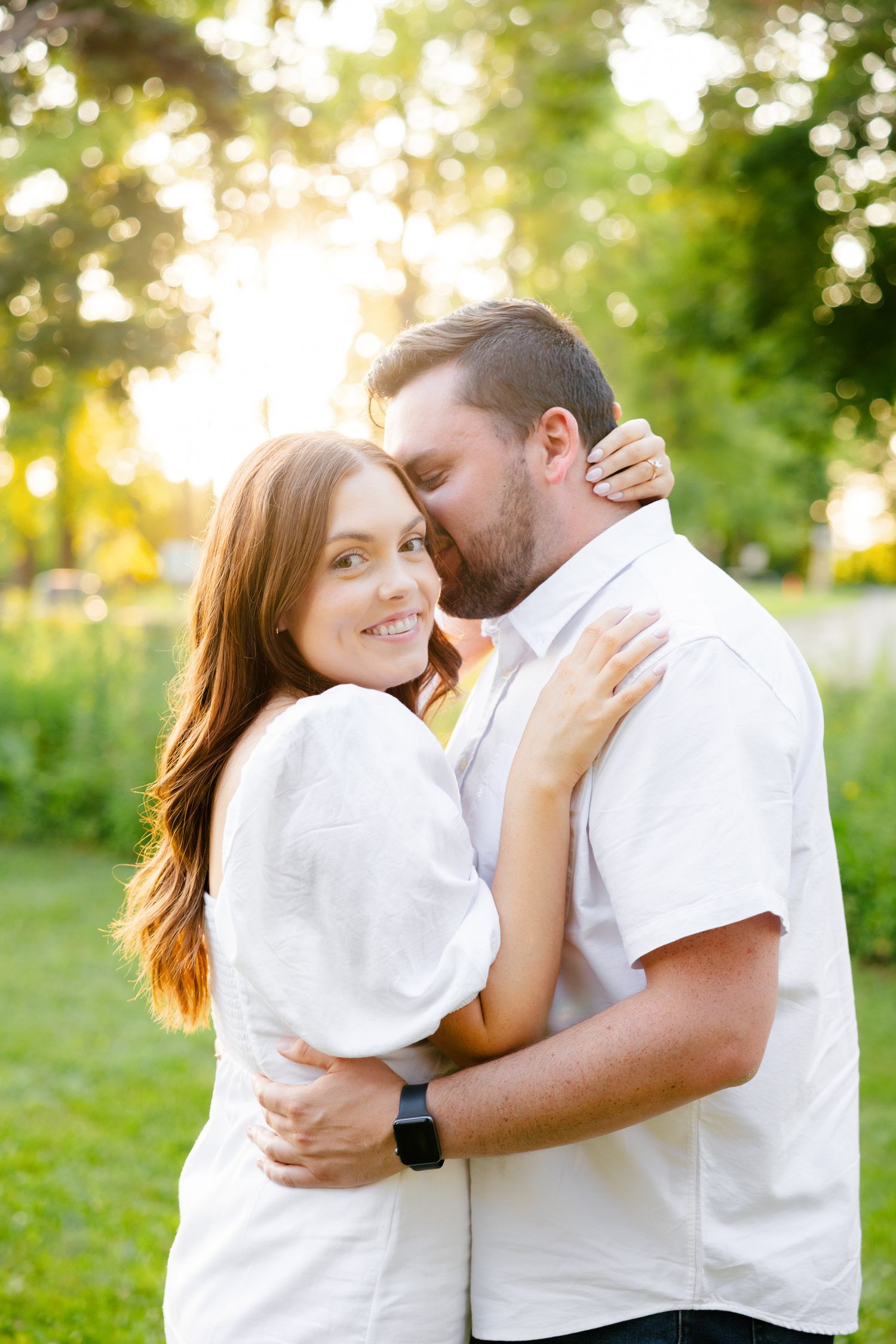 Romantic couple in white clothing embrace during golden hour in a lush garden setting.