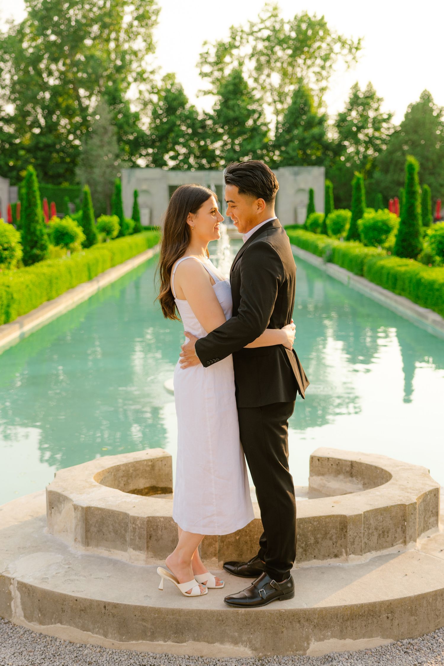 A romantic moment between a couple on stone steps with a reflecting pool in a formal garden.