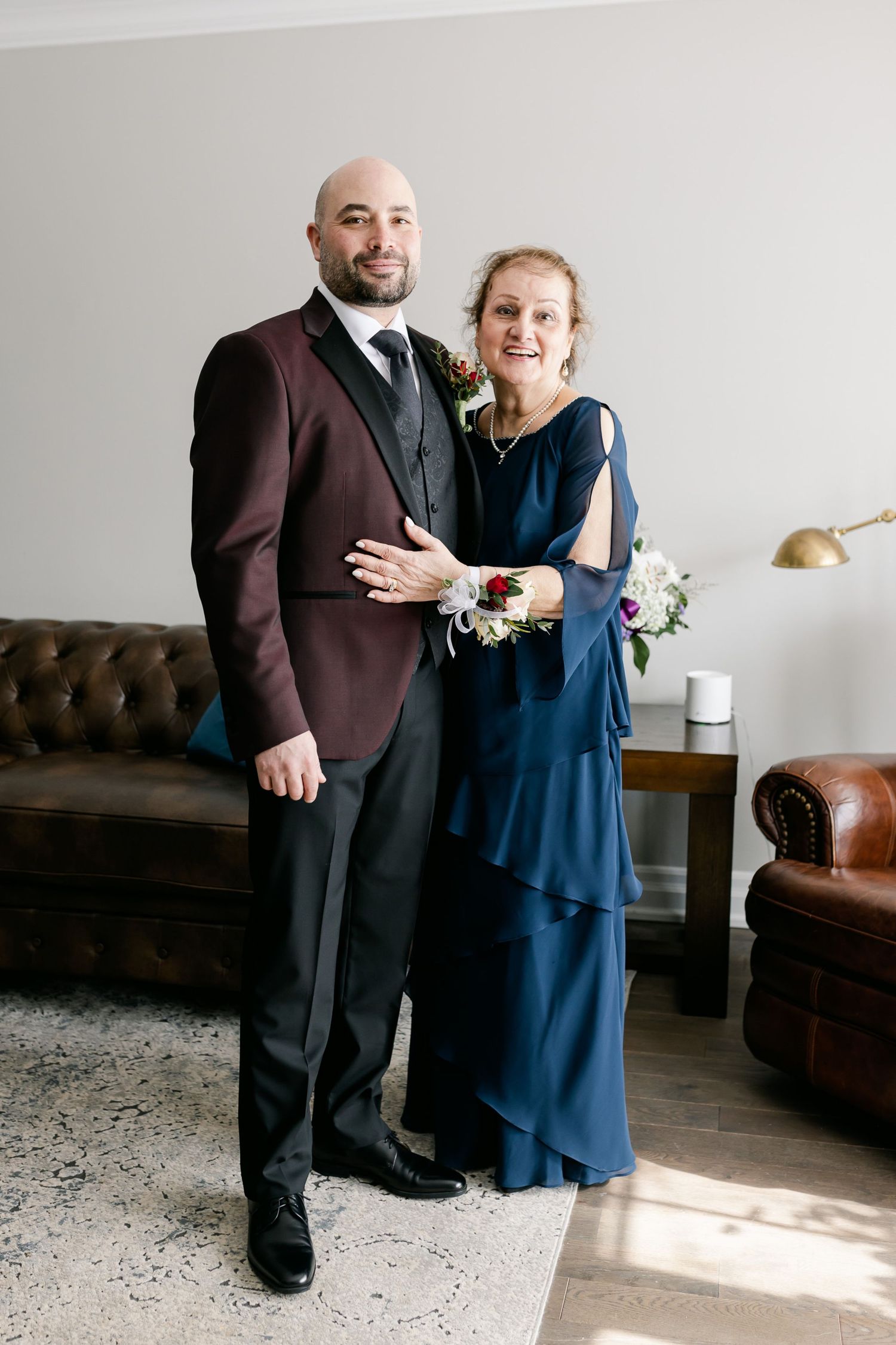 A formal portrait in front of a leather couch featuring burgundy jacket and navy dress.