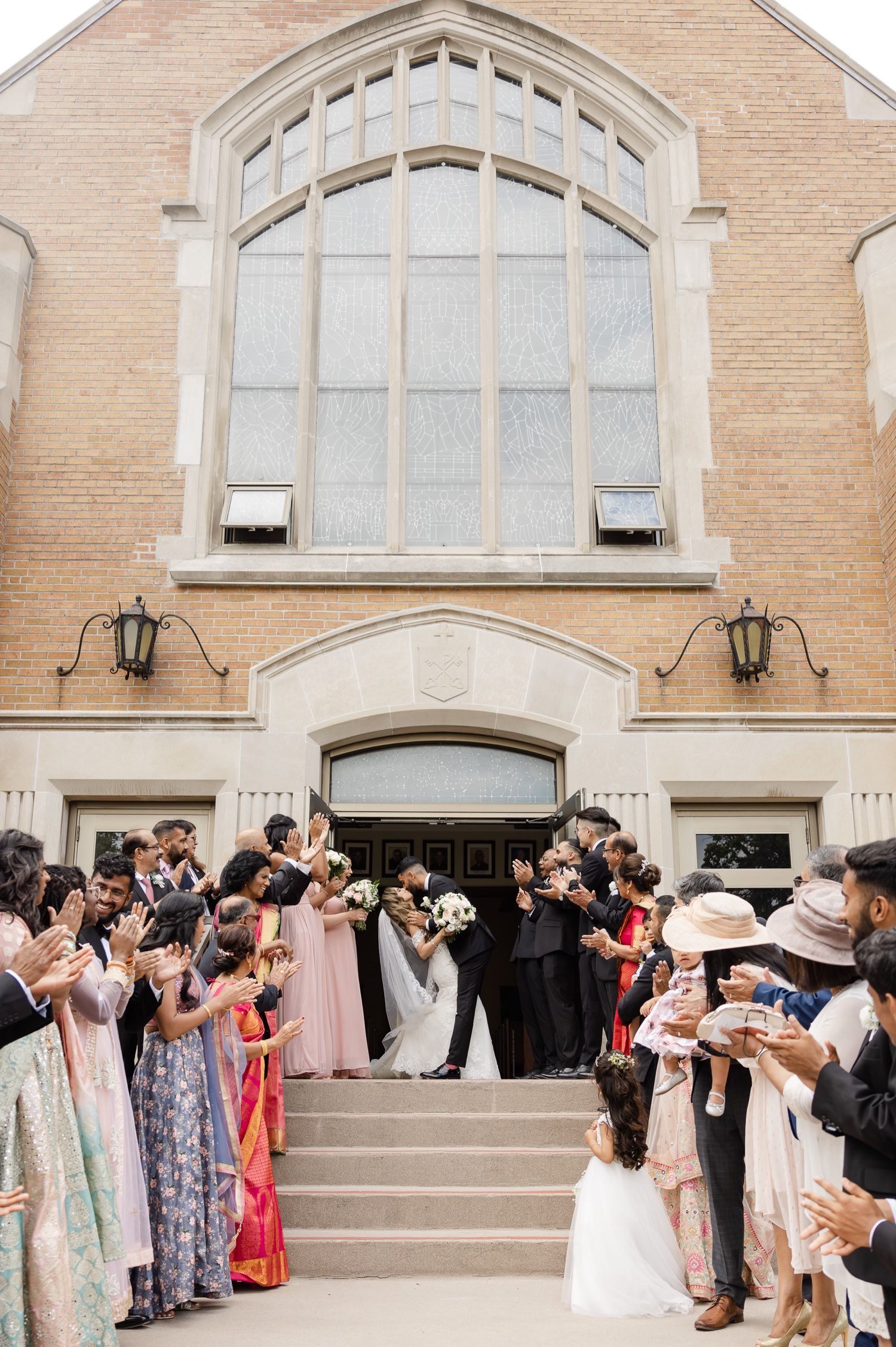 Joyful wedding celebration on church steps with guests in colorful attire.
