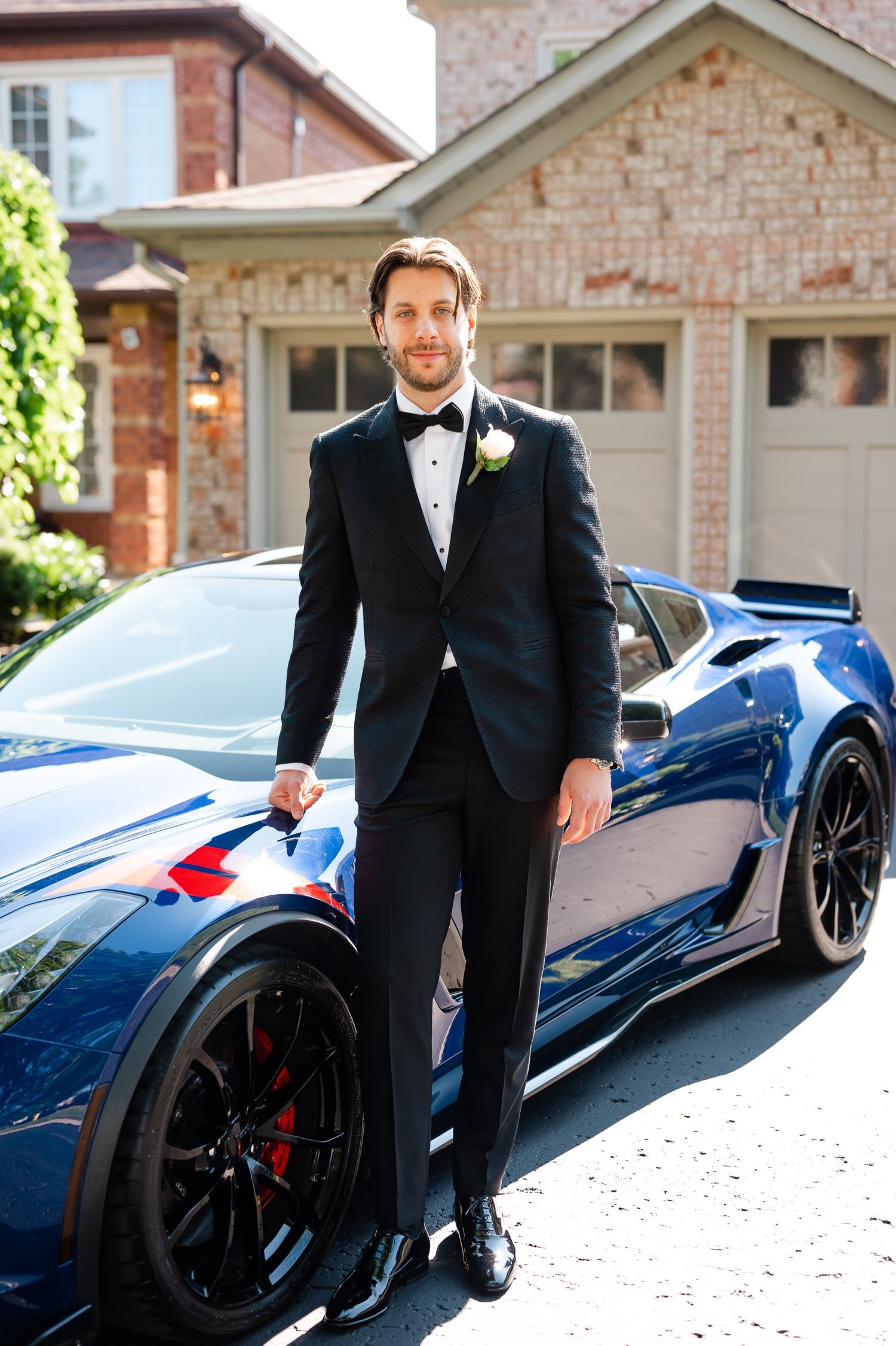 Elegant formal portrait with a blue luxury sports car in suburban driveway setting.
