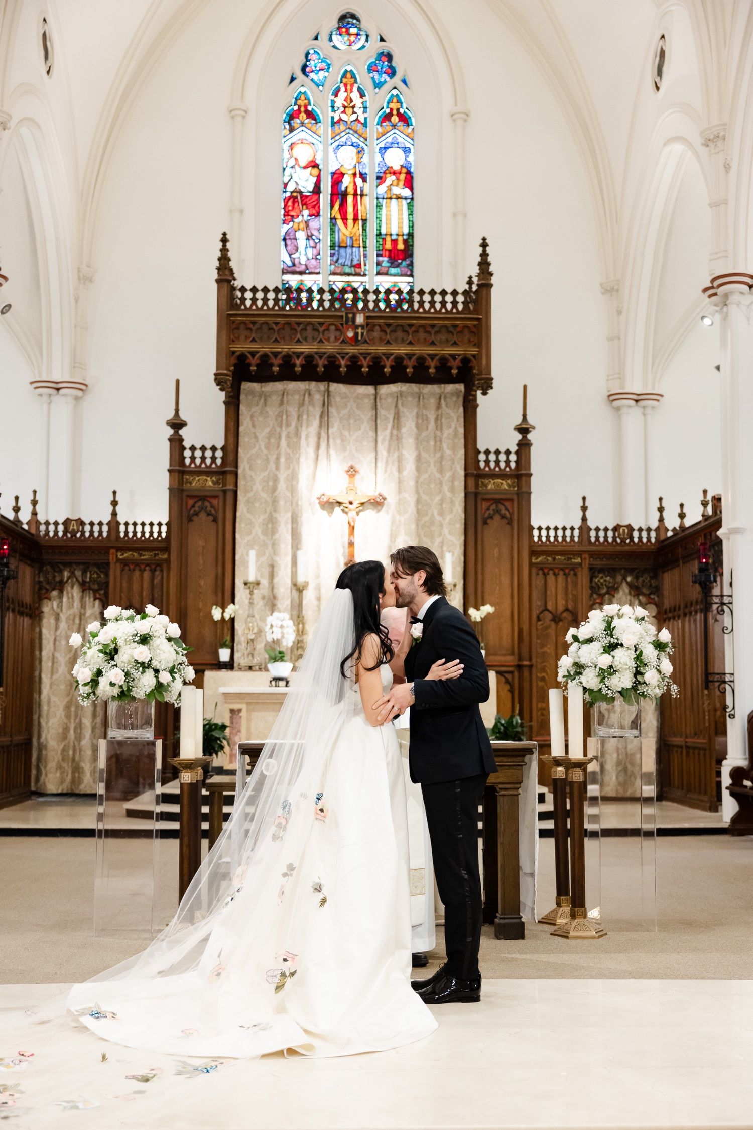 Elegant church wedding scene with stained glass windows and white floral arrangements framing the altar.