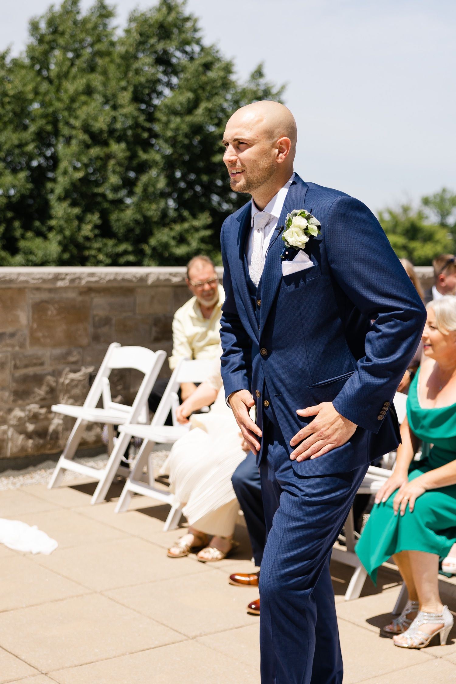Wedding ceremony setup outdoors with white chairs and guests seated on a stone patio.