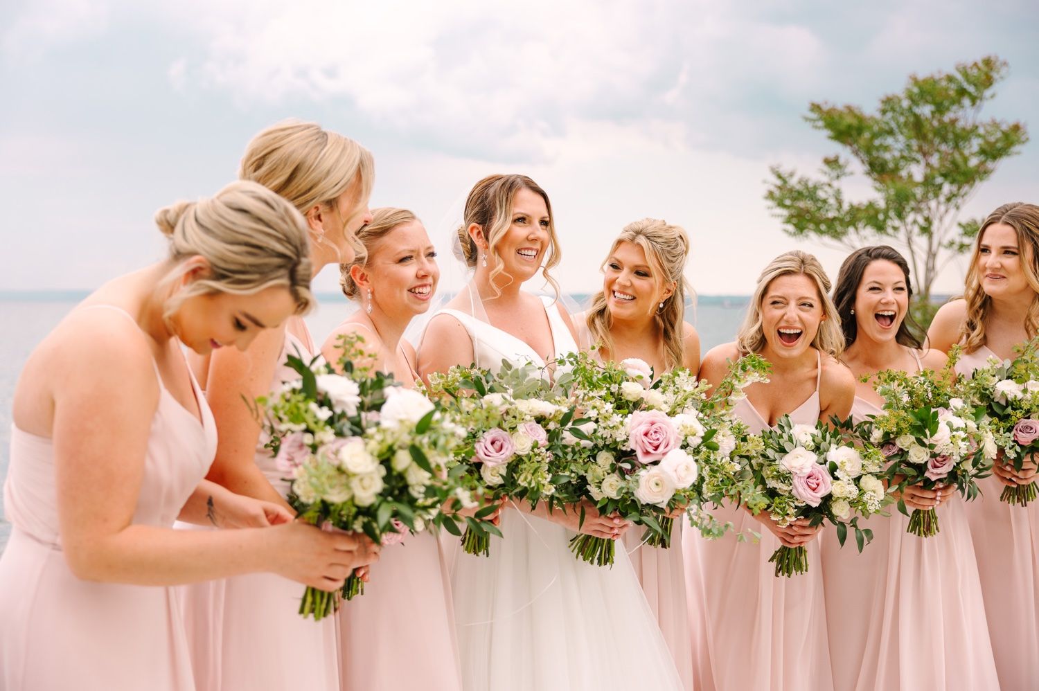 Group of bridesmaids share a candid laughing moment during wedding photos.