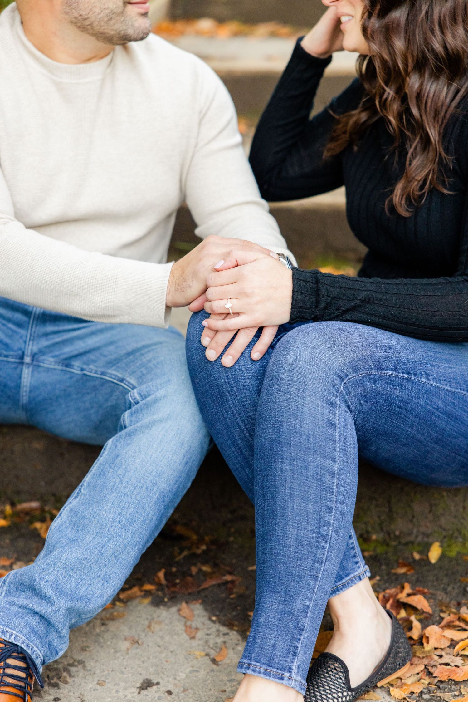 Close-up shot of intertwined hands resting on denim-clad legs on outdoor steps.