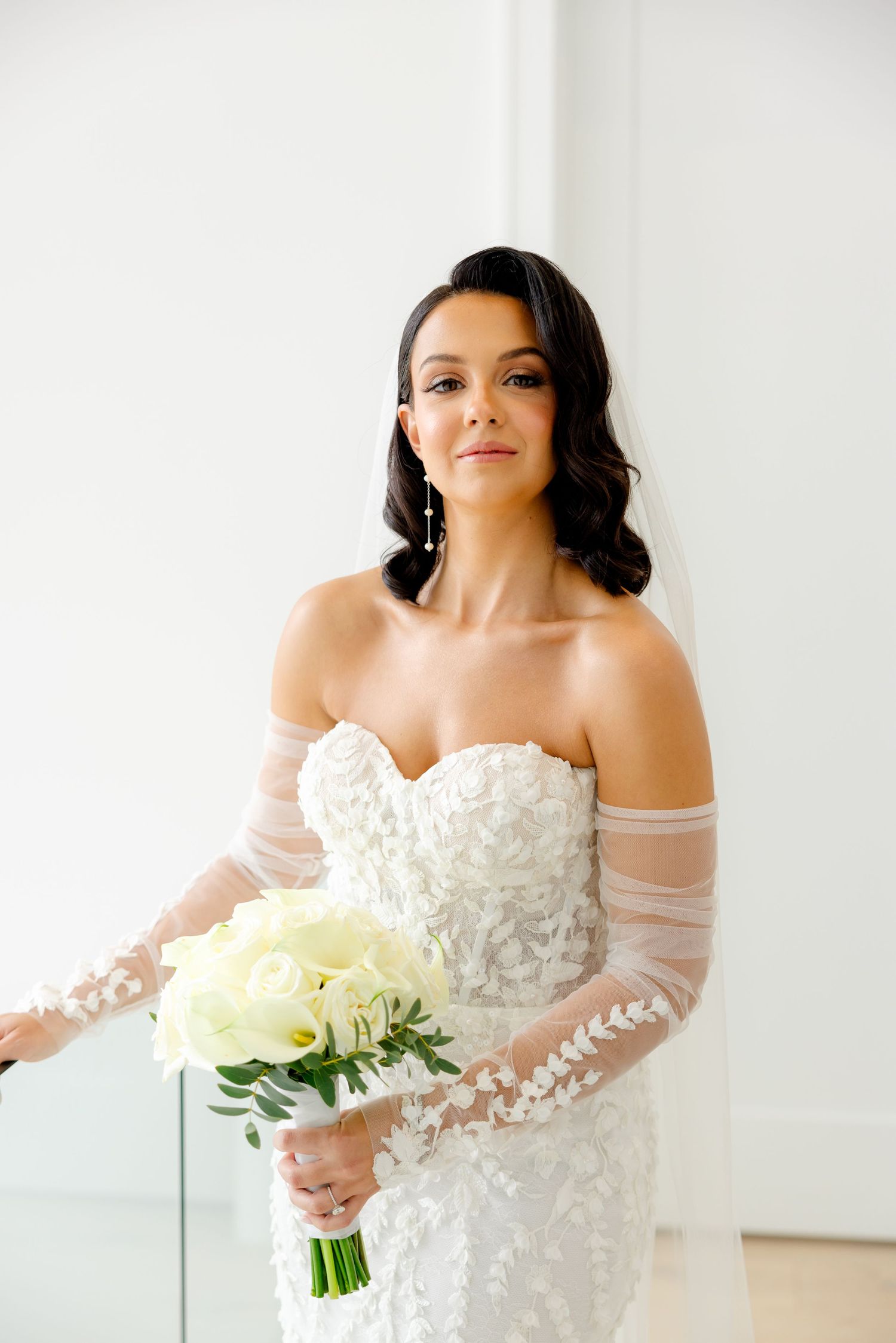 A close-up bridal portrait showcasing an off-shoulder lace gown paired with a white rose bouquet.