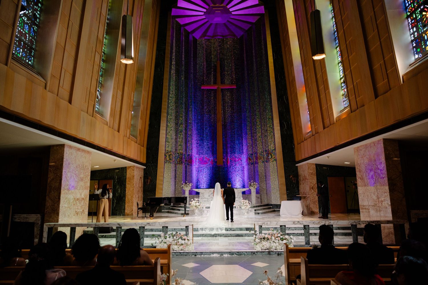 Modern church sanctuary with dramatic purple lighting and white marble steps during wedding ceremony.