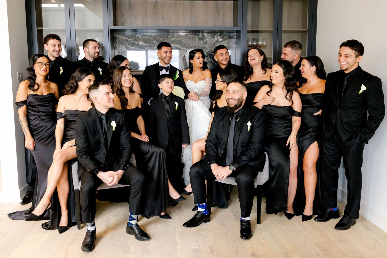 Large wedding party in coordinated black formal wear poses for a group photo.