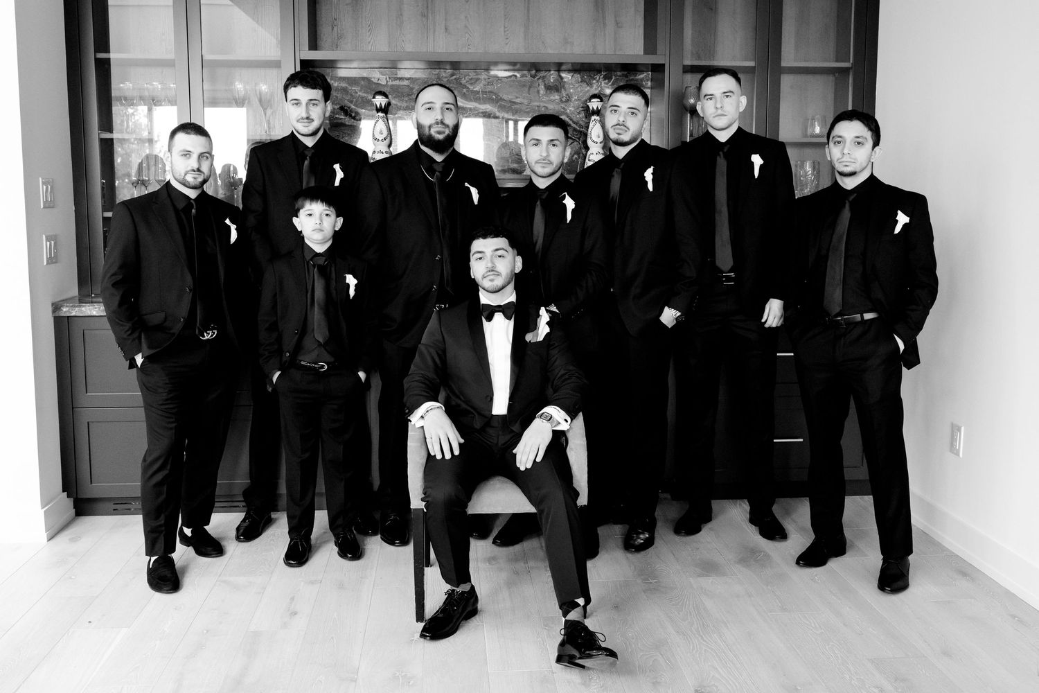 Groomsmen in black suits pose formally with one seated in center.