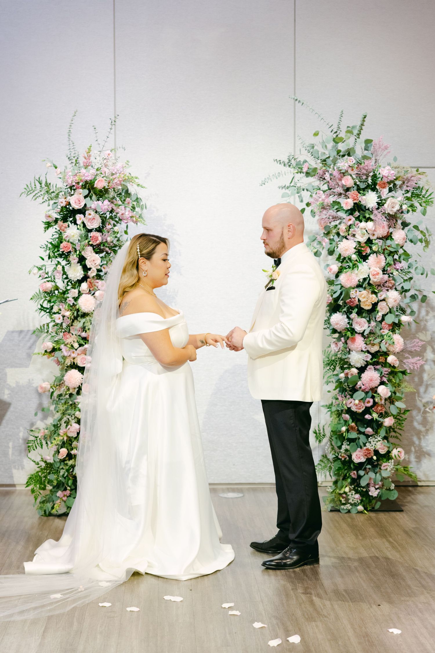 Intimate wedding moment under pink and white floral arches during ceremony.